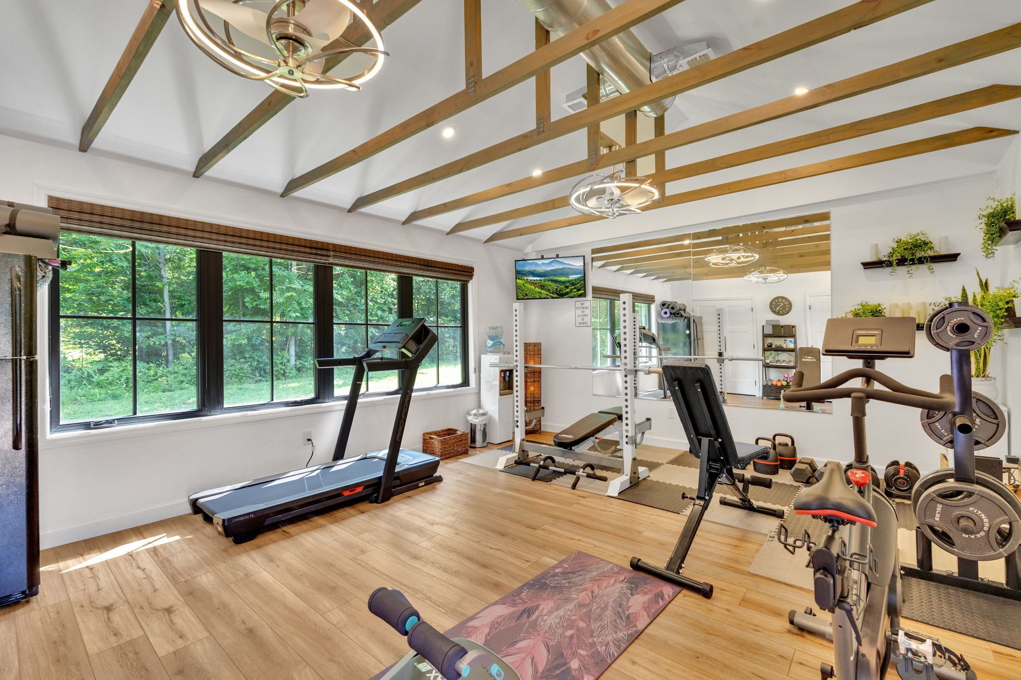 Ein großzügiger Fitnessraum mit Holzbalken, großen Fenstern und vielfältiger Trainingsausstattung.