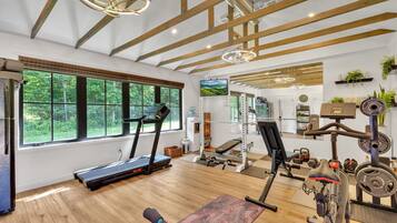 Ein großzügiger Fitnessraum mit Holzbalken, großen Fenstern und vielfältiger Trainingsausstattung.