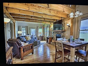 A spacious living room with a wooden ceiling, a fireplace, and a dining area with a table set for four. - Entire cabin in Maggie Valley (Maggie Valley)