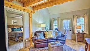 A cozy living room with a leather sofa, a wooden ceiling, and a bed in the adjacent room.