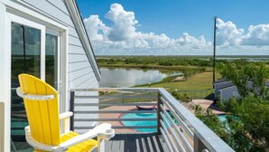 A balcony with a yellow chair, a pool, and a view of a lake and golf course. - Bayfront 2/2 Condo w/pool & Pier! Weekly Discounts (Rockport)