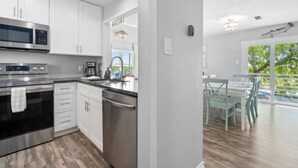 A modern kitchen with stainless steel appliances, white cabinetry, and a view to an outdoor dining area. - Bayfront 2/2 Condo w/pool & Pier! Weekly Discounts (Rockport)