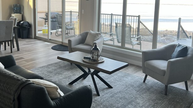 A spacious living room with a large sliding glass door leading to a balcony with a view of the beach.