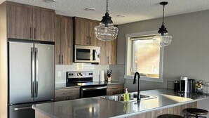 A modern kitchen with a large island, stainless steel appliances, wooden cabinets, and bar stools.