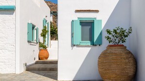Une ruelle étroite aux murs blancs et aux volets turquoise, qui mène à un escalier. Un grand pot en terre cuite contenant une plante est placé contre le mur.