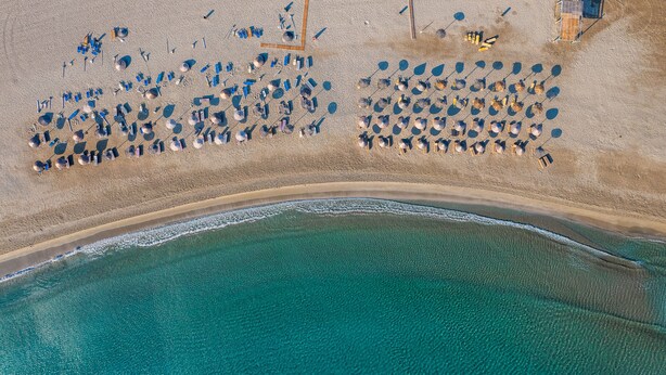 Vue aérienne d’une plage où de nombreux parasols et des chaises longues sont disposés en rangées.