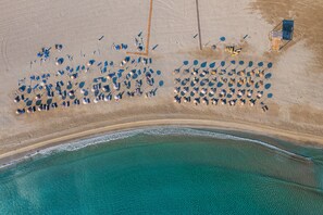 Vista aérea de uma praia com vários guarda-sóis e espreguiçadeiras dispostas em fileiras.