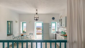 Une pièce avec un balcon, un coin repas comprenant des chaises et une table, une cuisine équipée de placards et d’un évier, et une vue sur le paysage par les fenêtres.