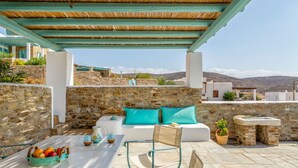 Une terrasse sur le toit avec un mur en pierre, un canapé blanc agrémenté de coussins turquoise, une table avec un panier de fruits et une vue sur le paysage.