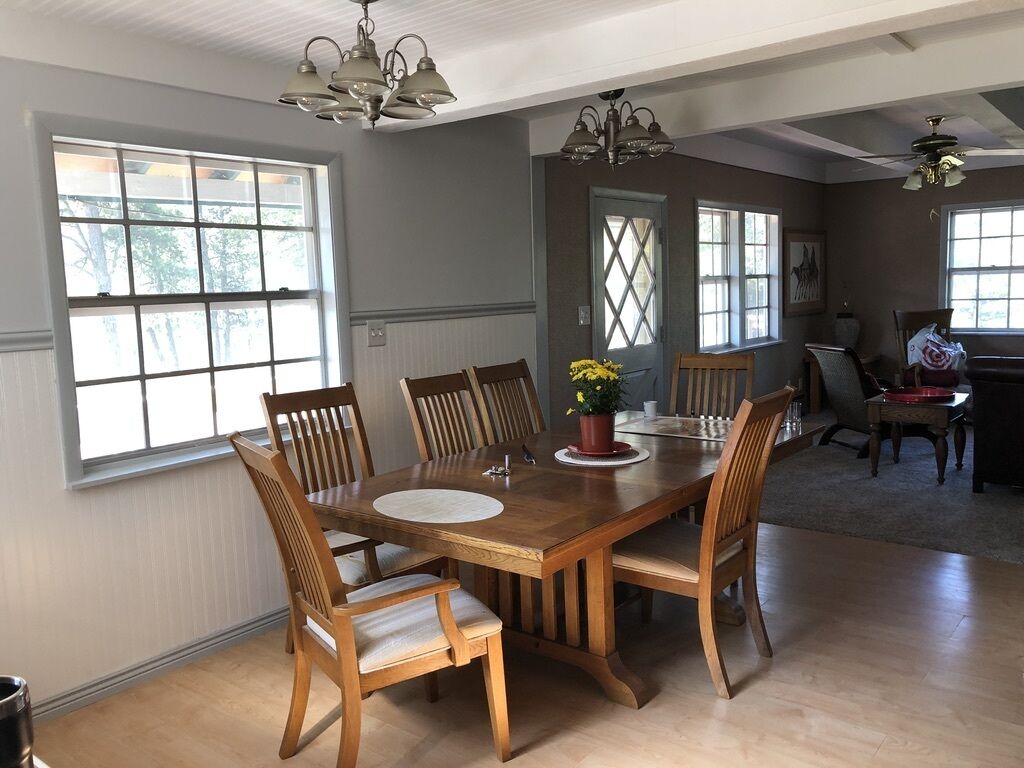 Un coin repas avec une table et des chaises en bois, de grandes fenêtres et un lustre.