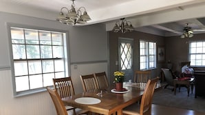 Uma área de refeições com mesa e cadeiras de madeira, janelas amplas e um lustre.