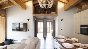 Una cocina moderna con vigas de madera, un comedor con mesa de madera dispuesta para cuatro personas y una lámpara colgante grande.