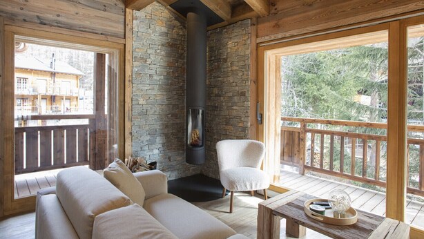 Interior acogedor de una cabaña con pared de piedra, chimenea, terraza de madera y sofá.