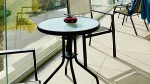 Een balkon met een glazen tafel en stoelen, met uitzicht op de kust.