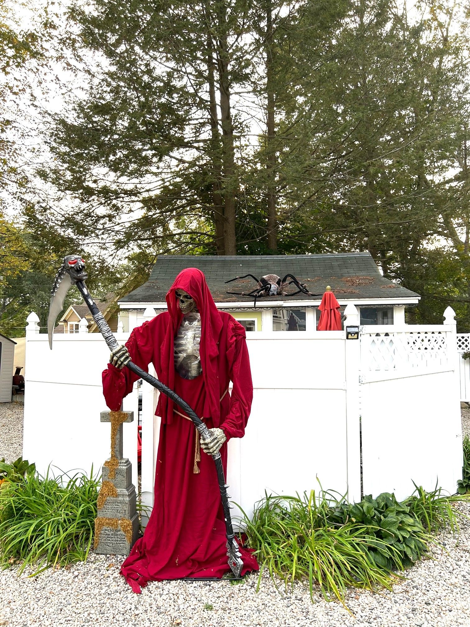 A statue of a figure in a red cloak holding a staff, standing in front of a white fence with greenery around.