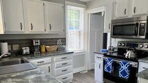 Una cocina con armarios blancos, horno de acero inoxidable, microondas y una ventana con persianas.