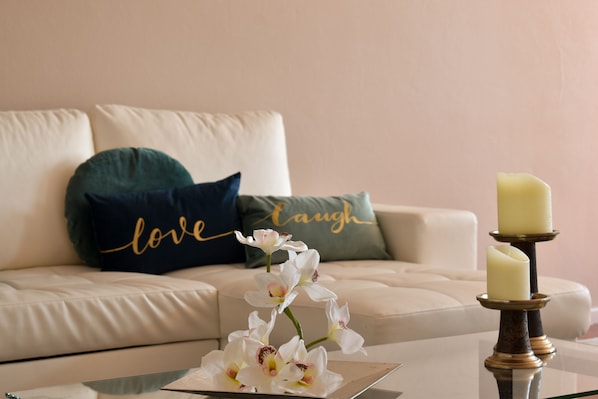 A living room with a white sofa, a green and blue pillow, a glass coffee table, and a candle holder with a candle.