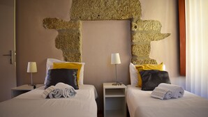 Two beds with white linens, yellow and black pillows, and rolled towels. There are bedside tables with lamps and a wall with a stone-like texture. - Apartment with 2 bedrooms, balcony and river view - 4th floor Registration no. 5848/AL (Porto)