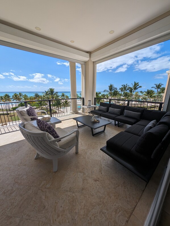 A spacious balcony with a view of the ocean, furnished with a sofa, chairs, and a coffee table. - Breathless Beauty, Oceanfront Condo 180 degree views (Punta Cana)