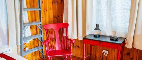 A room with a red chair, a small table with a lamp, and a ladder against a wooden wall.