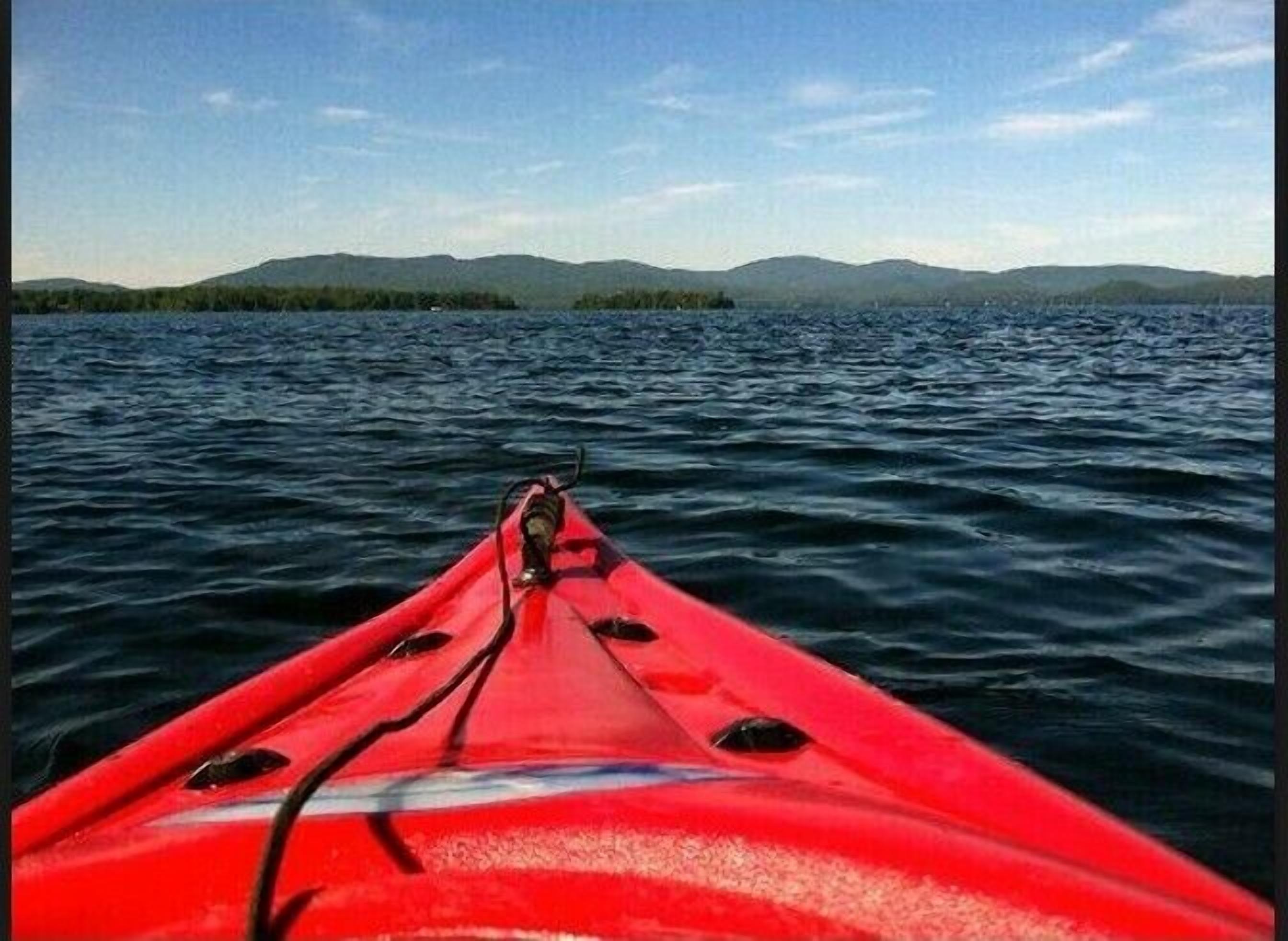 A red kayak on calm water with a distant view of mountains and a clear sky.