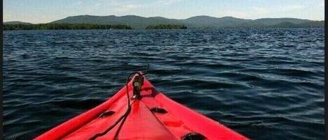 A red kayak on calm water with a distant view of mountains and a clear sky.