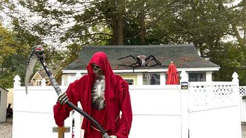 A statue of a figure in a red cloak holding a staff, standing in front of a white fence with greenery around.