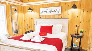 Une chambre d’hôtel avec un mur lambrissé en bois, un lit avec une literie blanche et un oreiller rouge, une table de chevet avec une lampe, et un panneau sur lequel on peut lire : « Faites de beaux rêves ».