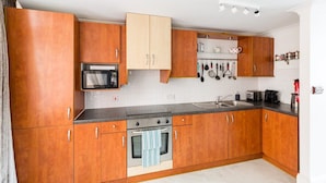 A kitchen with wooden cabinets, a microwave, an oven, and a sink. - City Centre Penthouse - New Street (Birmingham)