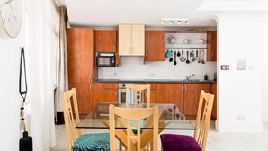 A modern kitchen with wooden cabinets, a microwave, and a glass dining table with chairs. - City Centre Penthouse - New Street (Birmingham)