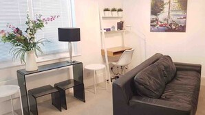 A modern living room with a black leather sofa, a glass coffee table, a white desk with a chair, a lamp, and a painting on the wall. - City Centre Penthouse - New Street (Birmingham)