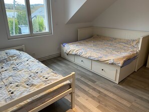 Quarto com duas camas, piso de madeira e janela com vista para casas.
