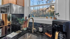 Una cocina moderna con una estufa de acero inoxidable, encimera de mármol negro, un fregadero y una ventana con vistas a árboles.