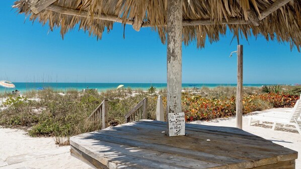 Una terraza de madera con techo de paja, con vista a una playa y agua azul cristalina.