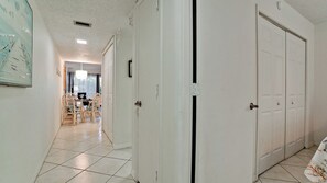 Un pasillo con piso de baldosas blancas, puertas blancas y un comedor con sillas de mimbre y una mesa.