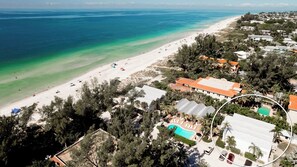 An aerial view of a coastal area with a beach, houses, and a pool.