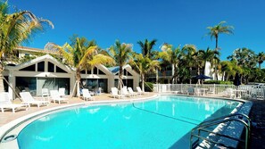 A swimming pool surrounded by lounge chairs and palm trees, with a building in the background.