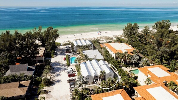 A resort with multiple buildings, a swimming pool, and a beach with clear turquoise waters.