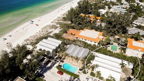 Vista aérea de una propiedad costera con playa, piscina y varias edificaciones con techos anaranjados.