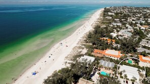 An aerial view of a coastal area with a beach, houses, and a pool.