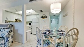 A compact living space with a dining area featuring a glass table and white wicker chairs. A kitchen with white cabinets and a refrigerator is visible in the background. - Coconuts 116 - Anna Maria Island - Condo -1 Bedroom/ 1 Bath- maximum occupancy of 6 people.     Distance to the Beach: 3 min walk  Community pool. (Holmes Beach)