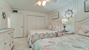 A bedroom with two beds, a dresser, a ceiling fan, a wall clock, and a lamp.