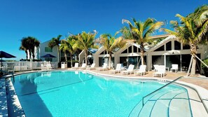 Una piscina con sillas de descanso y palmeras, rodeada de edificios con amplias ventanas.