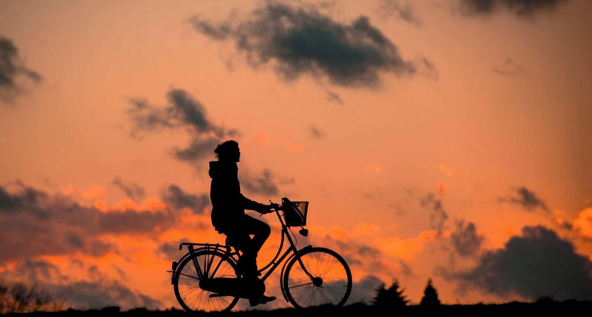 A silhouette of a person riding a bicycle against a sunset sky.