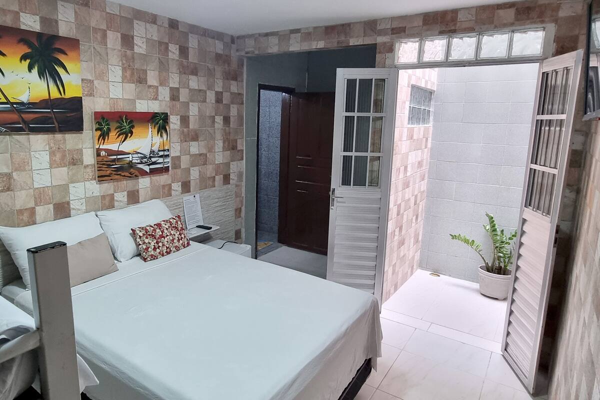 A bedroom with a bed, a nightstand, a wall-mounted TV, and a window with a view.