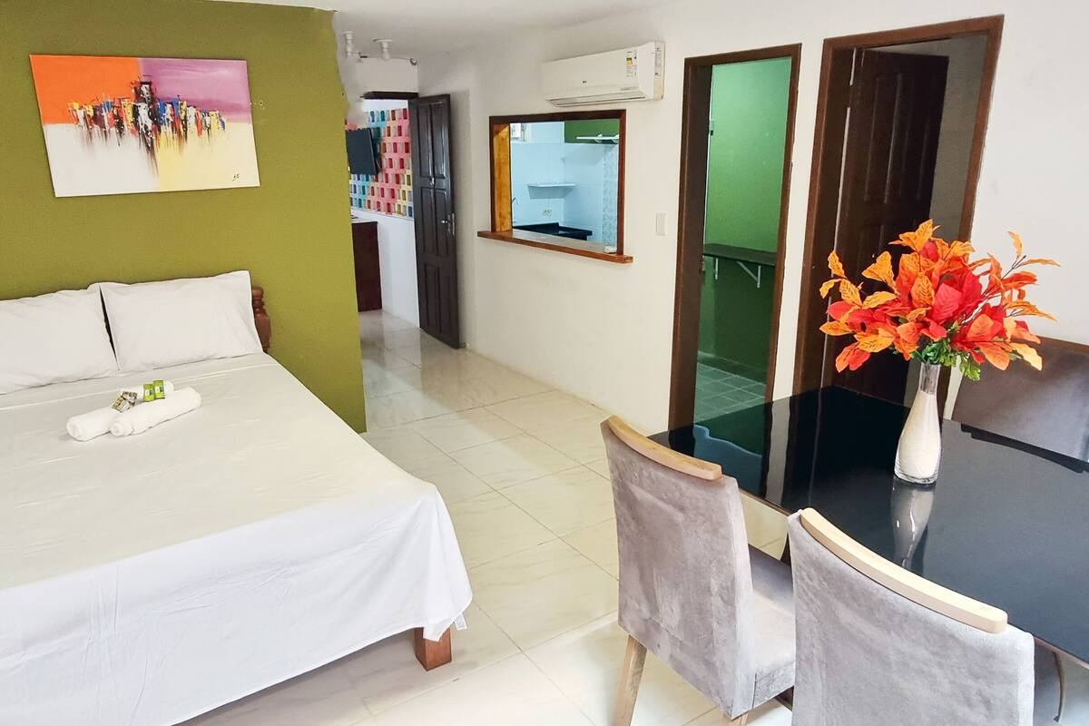 A hotel room with a bed, a desk, a chair, a vase with flowers, and a painting on the wall.