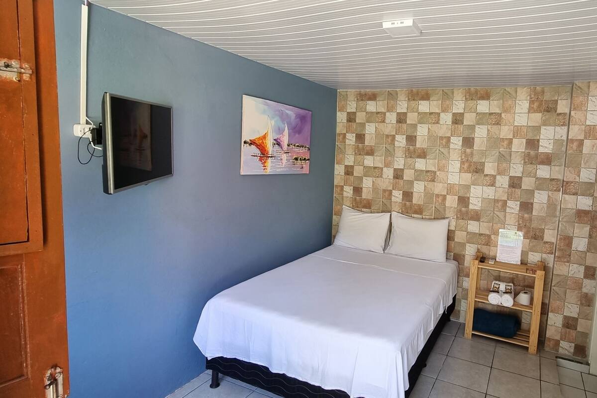 A bedroom with a bed, a TV, a painting, a checkered wall, and an air conditioning unit.