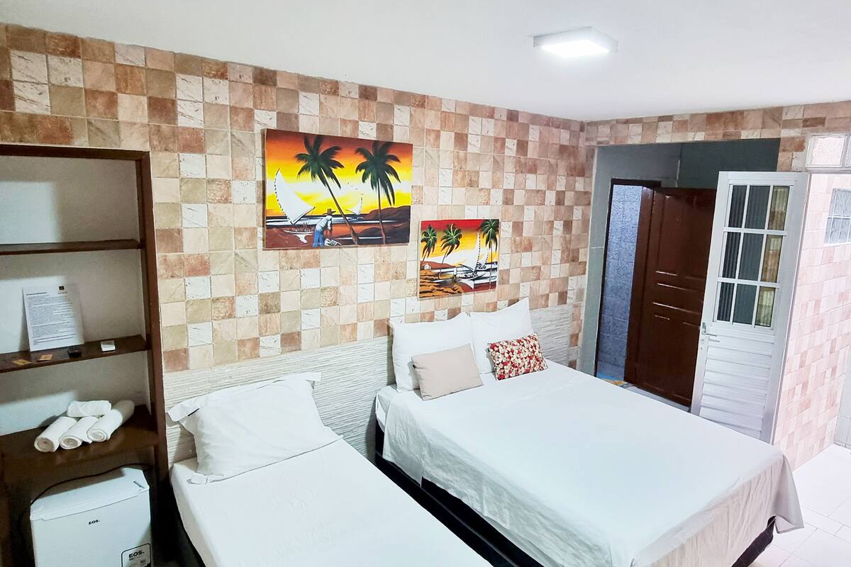 A hotel room with a checkered wall pattern, a bed with white bedding, a shelf with towels, and two paintings depicting tropical scenes.