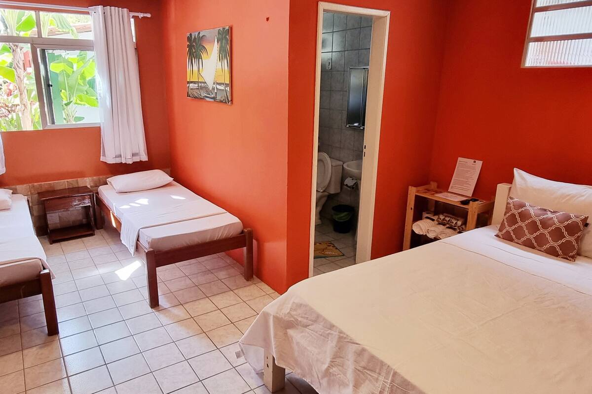 A hotel room with two single beds, a large bed, and a wooden nightstand with a lamp.