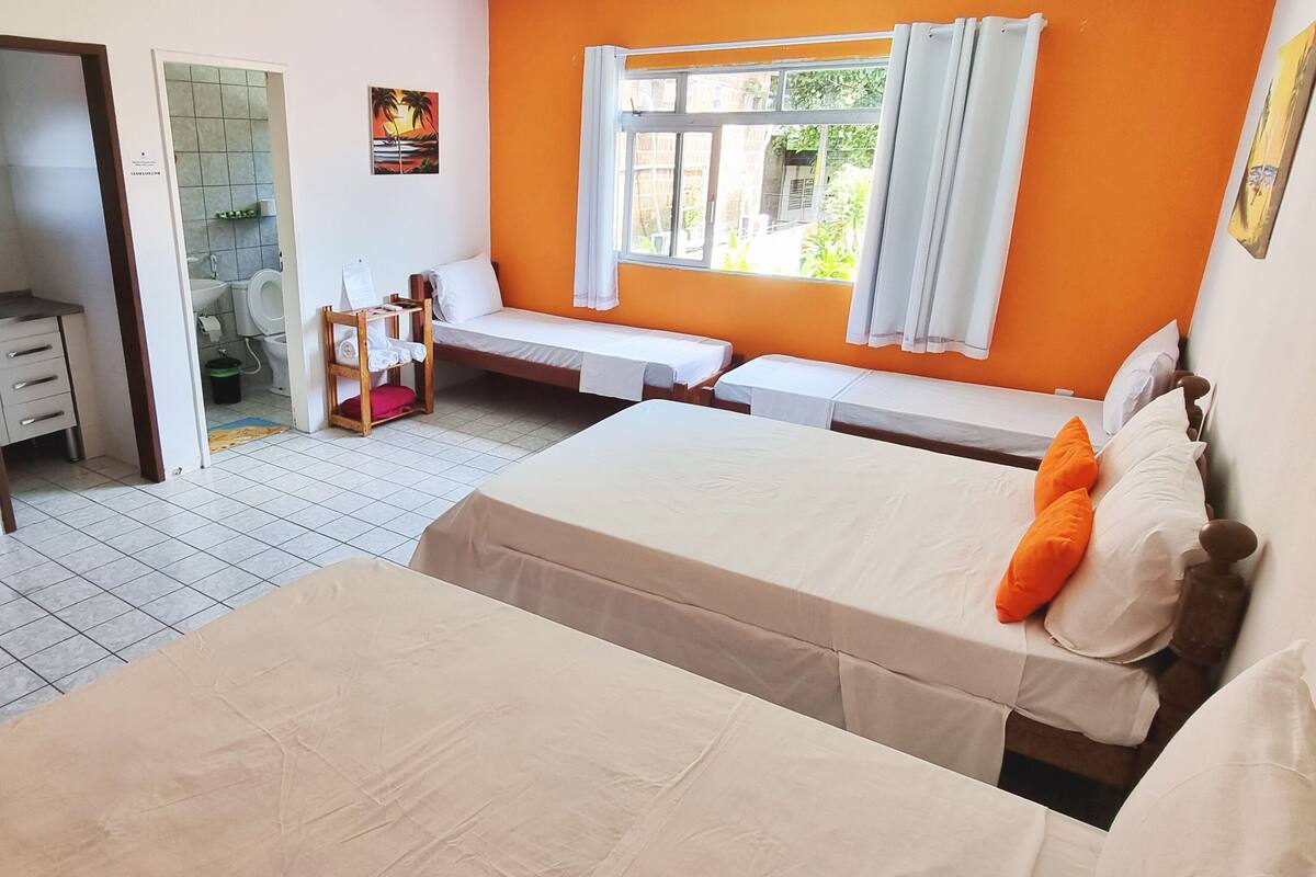 A bedroom with two beds, a small sitting area, a window with curtains, and a view of the outside.